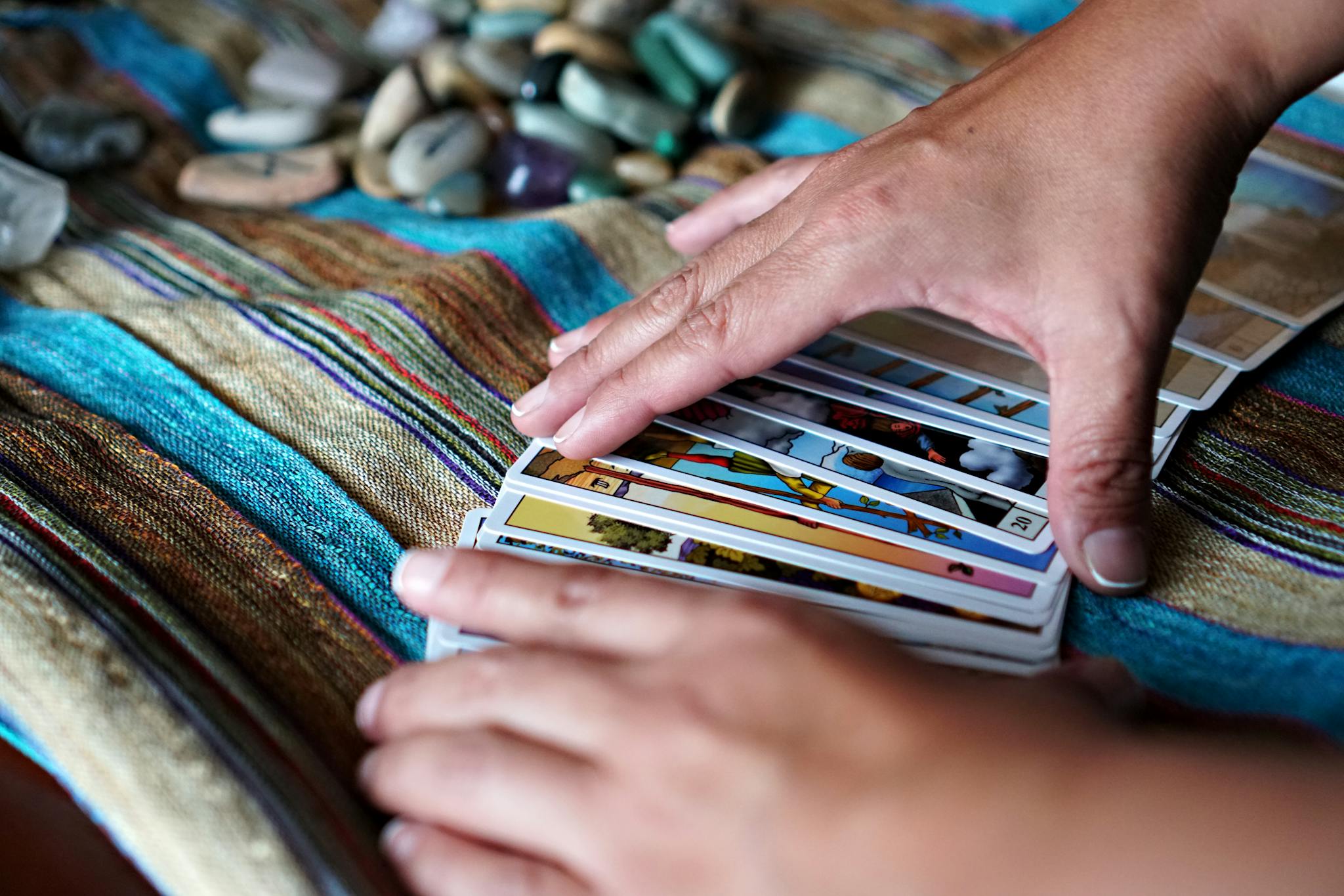 Hands arranging tarot cards on a vibrant cloth with gemstones, creating a mystical atmosphere.