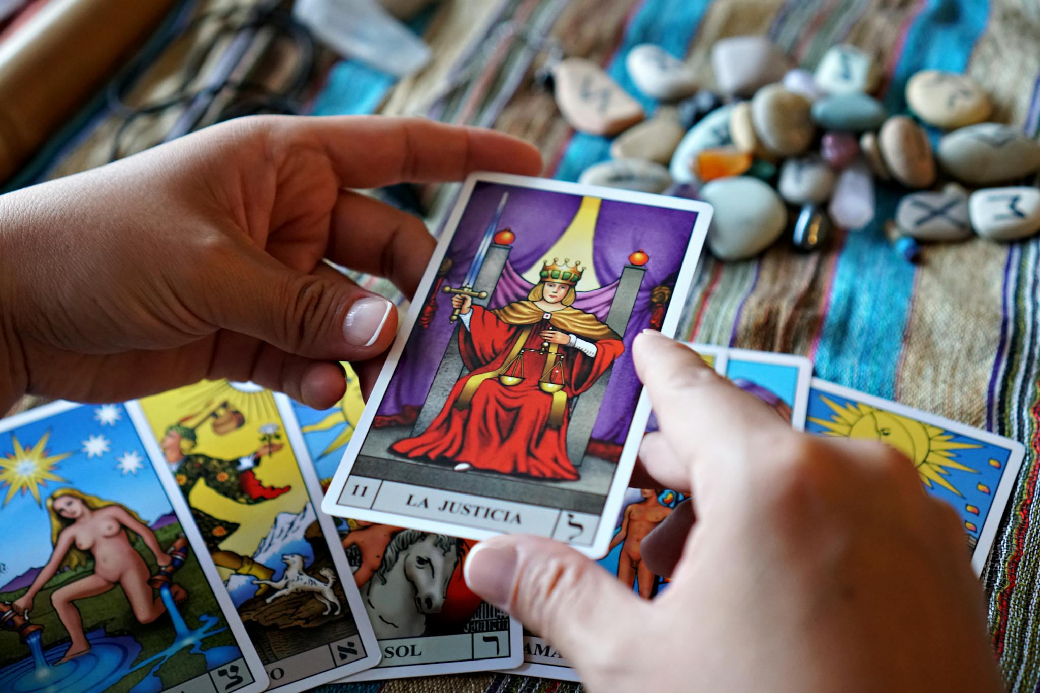 Hands holding a tarot card of justice over a colorful cloth during a reading.
